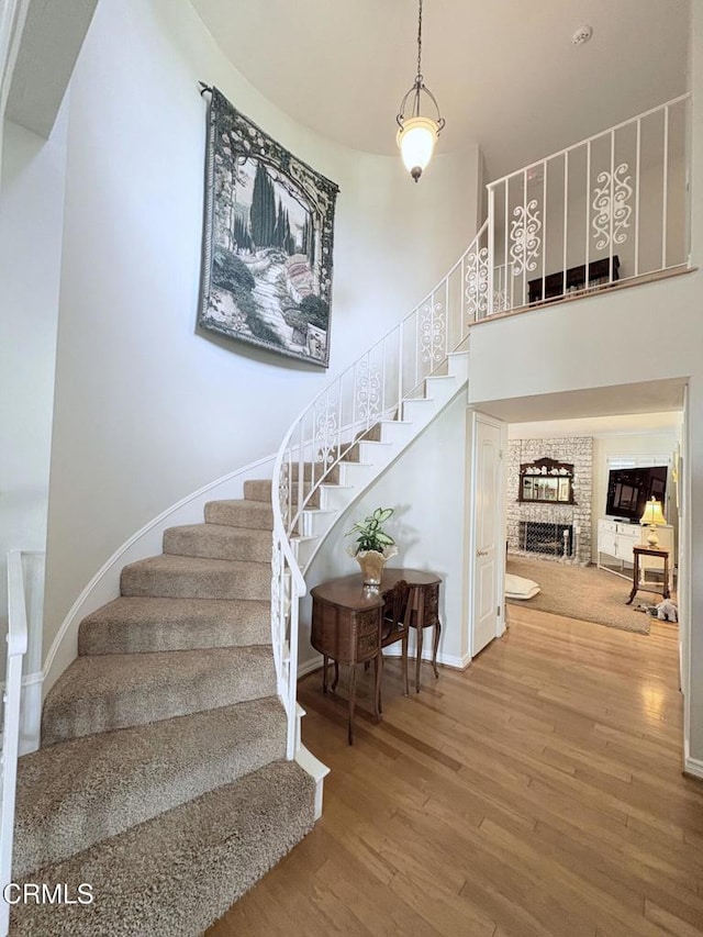 stairway featuring wood-type flooring, a towering ceiling, and a fireplace