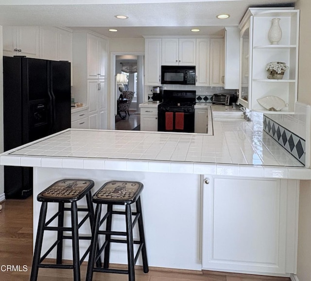 kitchen featuring tile counters, white cabinets, kitchen peninsula, and black appliances