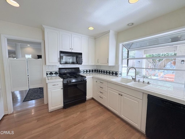 kitchen with sink, white cabinetry, black appliances, and tile counters