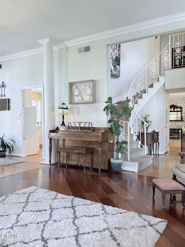 living area featuring wood finished floors, visible vents, ornate columns, ornamental molding, and stairs