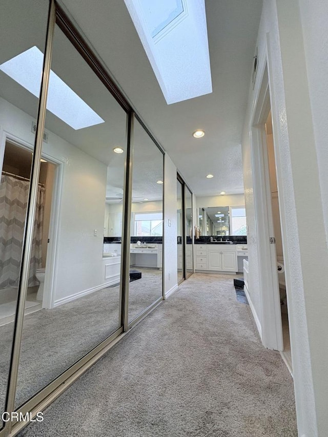 hallway featuring baseboards, a healthy amount of sunlight, a skylight, and carpet