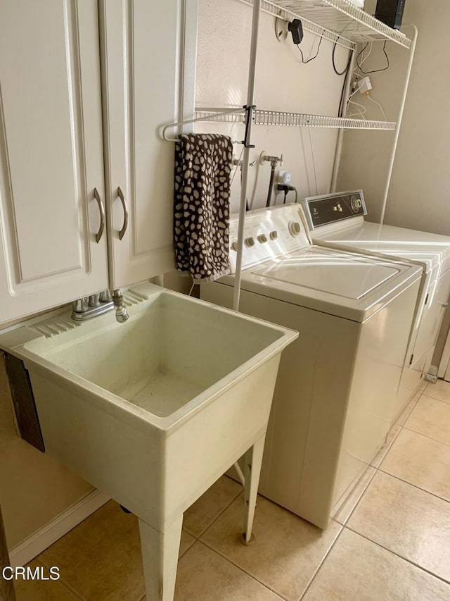 clothes washing area with a sink, light tile patterned floors, cabinet space, and washer and clothes dryer