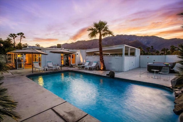 pool at dusk with a mountain view, a jacuzzi, a patio, and a gazebo