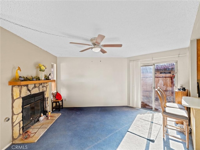 carpeted living room with ceiling fan, a stone fireplace, and a textured ceiling