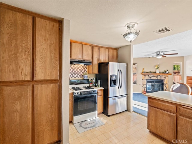 kitchen featuring a fireplace, white range with gas stovetop, ceiling fan, stainless steel refrigerator with ice dispenser, and a textured ceiling