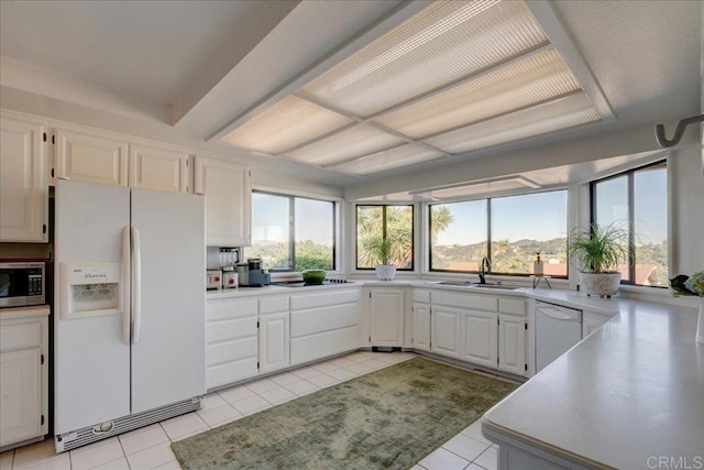 kitchen with light tile patterned floors, white appliances, sink, and white cabinets