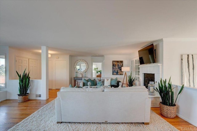 living room with ornamental molding, a brick fireplace, and light hardwood / wood-style floors