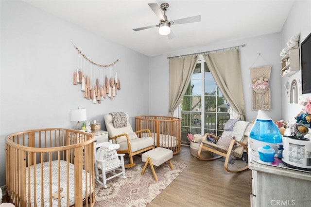 bedroom featuring hardwood / wood-style flooring, ceiling fan, and a crib