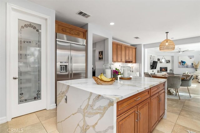 kitchen with decorative light fixtures, ceiling fan, a center island, stainless steel built in refrigerator, and light stone counters