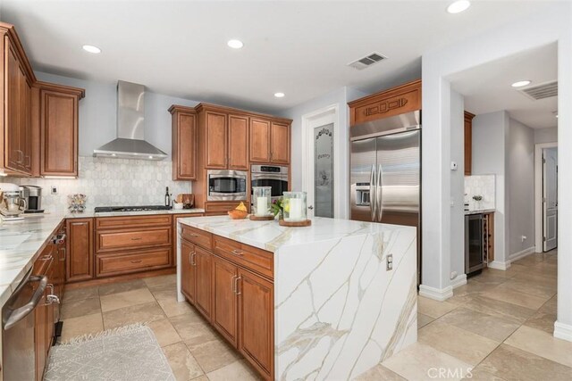 kitchen featuring backsplash, light stone countertops, a kitchen island, wall chimney exhaust hood, and built in appliances