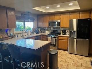 kitchen featuring sink, a breakfast bar area, appliances with stainless steel finishes, a tray ceiling, and kitchen peninsula