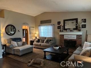 living room featuring wood-type flooring, vaulted ceiling, and a brick fireplace