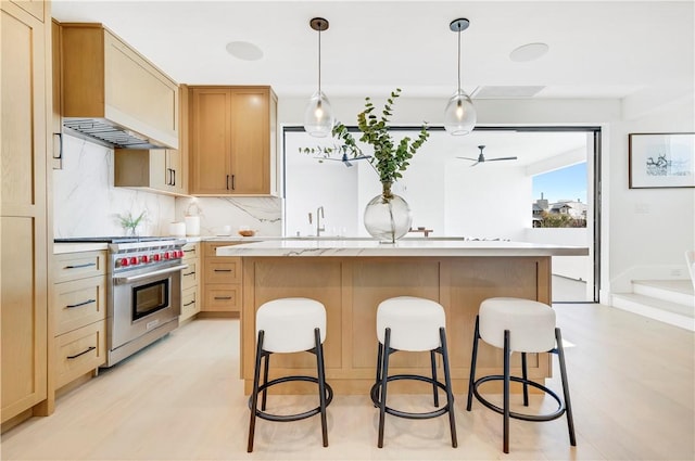 kitchen featuring decorative backsplash, high end stainless steel range, a kitchen island with sink, and ceiling fan