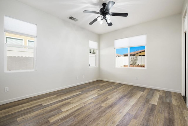 empty room with ceiling fan, a healthy amount of sunlight, and dark wood-type flooring