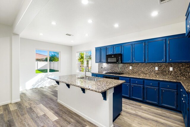 kitchen with a kitchen island with sink, blue cabinetry, dark stone counters, and black appliances