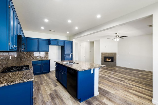 kitchen featuring black appliances, decorative backsplash, sink, a kitchen island with sink, and blue cabinets