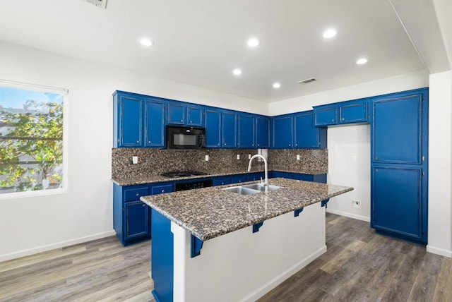 kitchen with a center island with sink, a breakfast bar area, dark stone countertops, black appliances, and sink