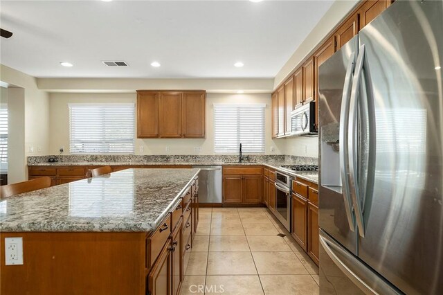 kitchen featuring a kitchen island, light stone countertops, sink, and appliances with stainless steel finishes