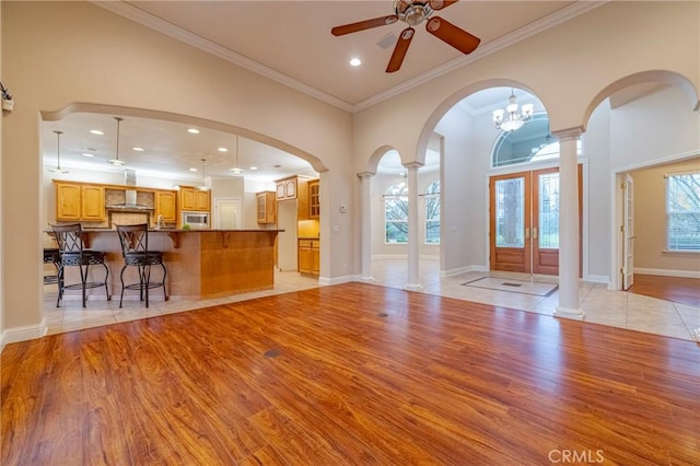 unfurnished living room featuring ceiling fan with notable chandelier, light hardwood / wood-style flooring, ornamental molding, and french doors