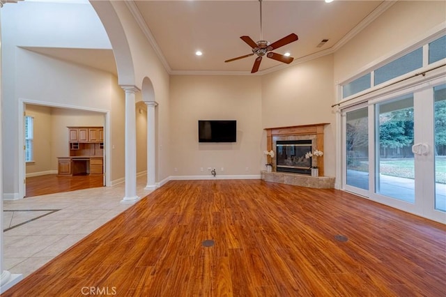 unfurnished living room featuring light tile patterned floors, decorative columns, ceiling fan, crown molding, and a tile fireplace