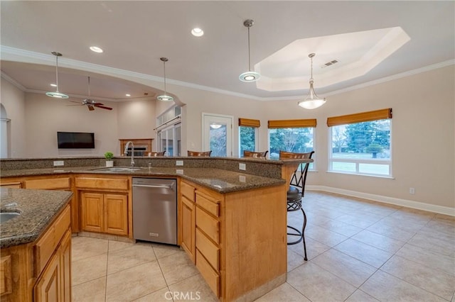 kitchen with ceiling fan, a tray ceiling, hanging light fixtures, stainless steel dishwasher, and a breakfast bar