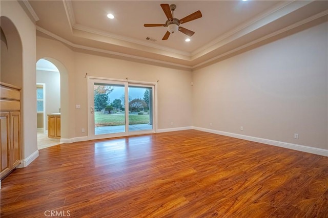 empty room with ceiling fan, ornamental molding, light hardwood / wood-style flooring, and a raised ceiling