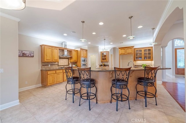 kitchen featuring a spacious island, a breakfast bar, crown molding, hanging light fixtures, and wall chimney exhaust hood