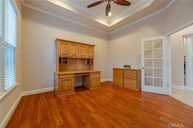 unfurnished office with light wood-type flooring, ceiling fan, crown molding, and a raised ceiling