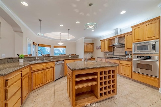 kitchen featuring wall chimney exhaust hood, decorative light fixtures, stainless steel appliances, an island with sink, and sink