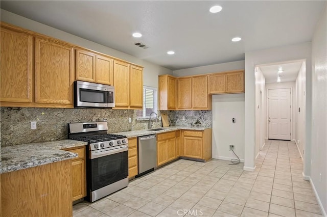 kitchen with appliances with stainless steel finishes, tasteful backsplash, light stone counters, and sink