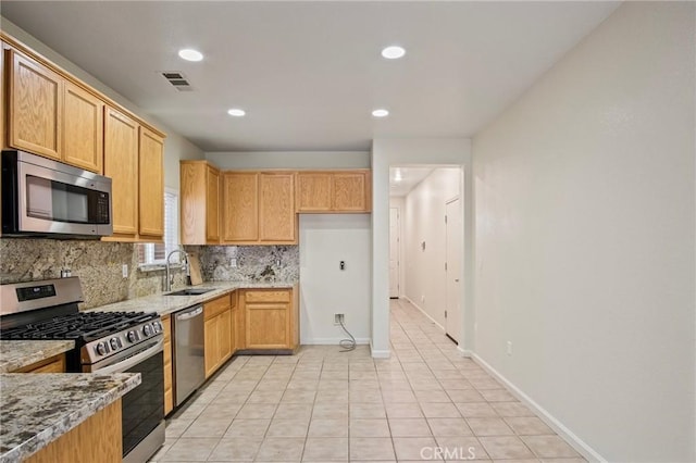 kitchen with decorative backsplash, sink, light stone countertops, appliances with stainless steel finishes, and light tile patterned floors