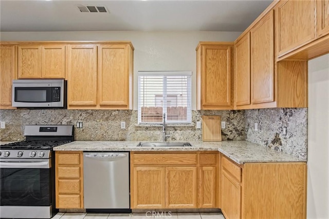 kitchen with appliances with stainless steel finishes, decorative backsplash, light stone counters, and sink