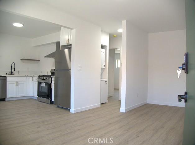 kitchen featuring white cabinetry, sink, wall chimney range hood, light hardwood / wood-style floors, and appliances with stainless steel finishes