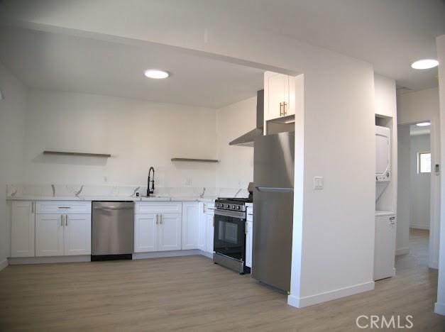 kitchen featuring wall chimney range hood, light hardwood / wood-style floors, sink, white cabinetry, and stainless steel appliances