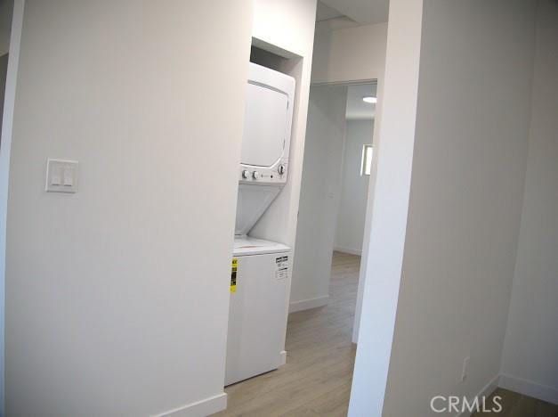 washroom with stacked washing maching and dryer and light wood-type flooring