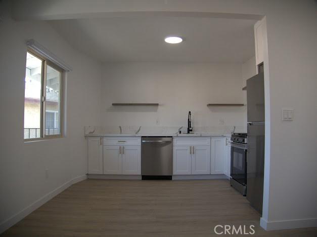 kitchen with white cabinets, range with gas stovetop, sink, light wood-type flooring, and stainless steel dishwasher