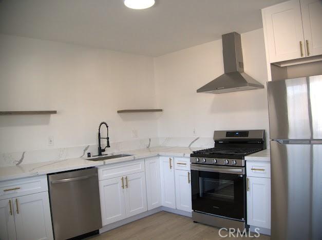 kitchen featuring appliances with stainless steel finishes, white cabinets, wall chimney range hood, light hardwood / wood-style floors, and sink