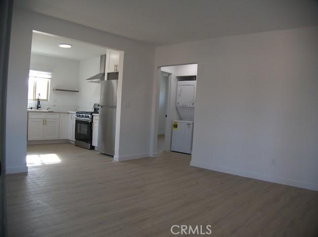 kitchen with white cabinetry, light hardwood / wood-style floors, stainless steel appliances, wall chimney exhaust hood, and sink