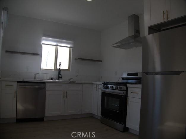 kitchen featuring white cabinets, wall chimney range hood, appliances with stainless steel finishes, and sink