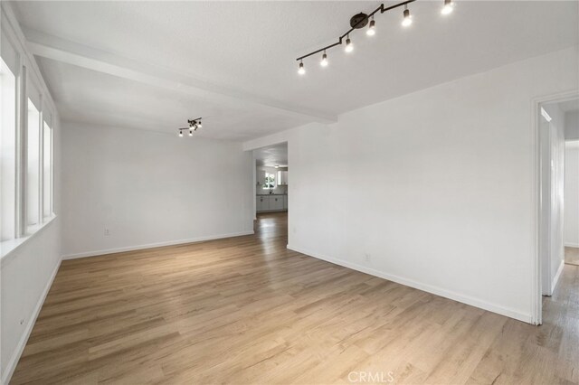 spare room with light hardwood / wood-style floors, a healthy amount of sunlight, and beamed ceiling