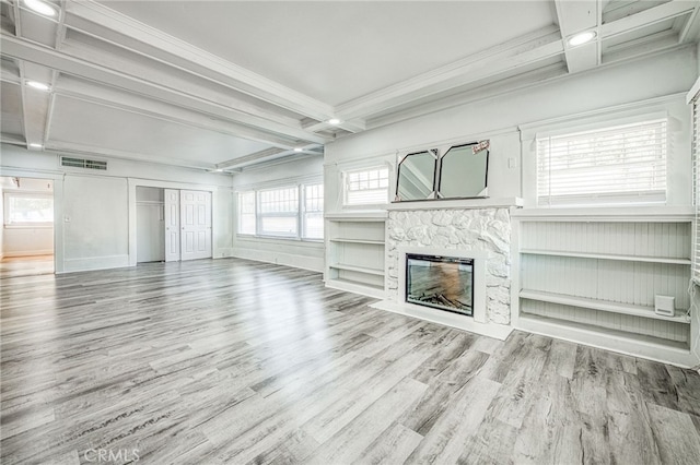 unfurnished living room featuring light wood-type flooring, crown molding, beam ceiling, and a stone fireplace