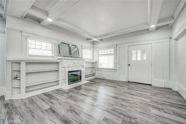 unfurnished living room featuring coffered ceiling, a stone fireplace, ornamental molding, light hardwood / wood-style flooring, and beamed ceiling