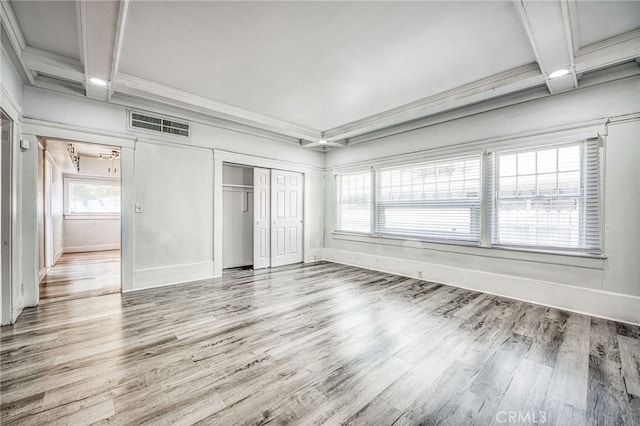 unfurnished bedroom with beam ceiling, a closet, crown molding, and hardwood / wood-style flooring