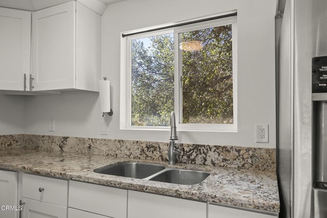 kitchen featuring sink, light stone countertops, stainless steel fridge with ice dispenser, and white cabinets