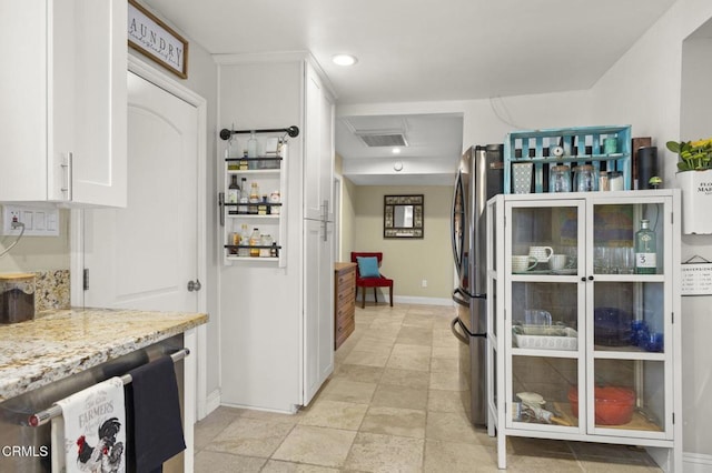 kitchen with light stone counters, stainless steel refrigerator, and white cabinets