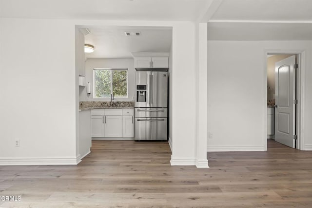 kitchen featuring white cabinetry, sink, stainless steel fridge, light stone countertops, and light wood-type flooring