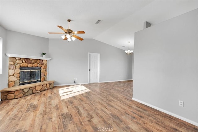 unfurnished living room with lofted ceiling, ceiling fan with notable chandelier, a stone fireplace, and hardwood / wood-style flooring