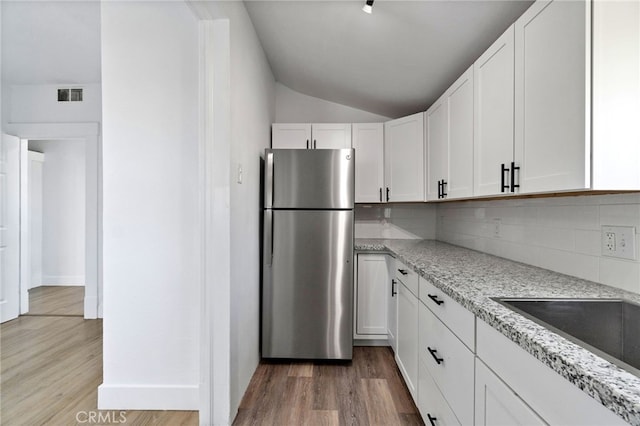 kitchen featuring white cabinetry, decorative backsplash, stainless steel refrigerator, light wood-type flooring, and light stone counters