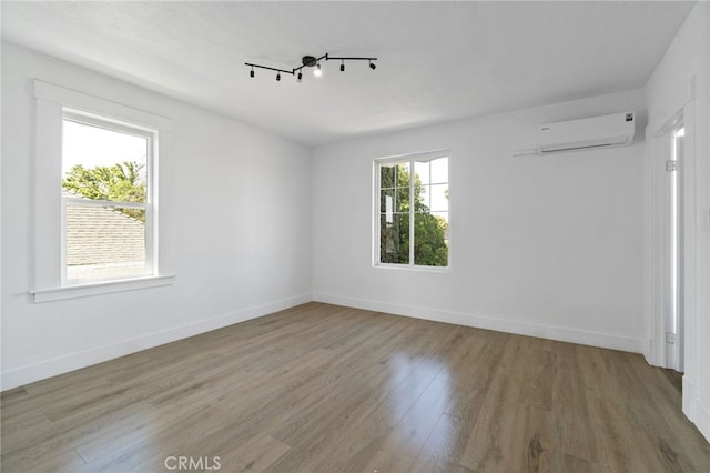 spare room featuring wood-type flooring, track lighting, and a wall mounted air conditioner