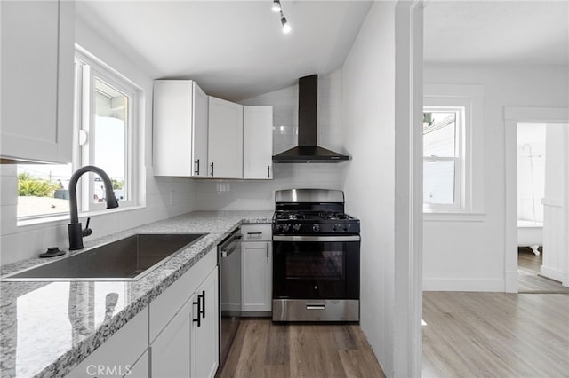 kitchen with sink, white cabinetry, appliances with stainless steel finishes, and wall chimney exhaust hood